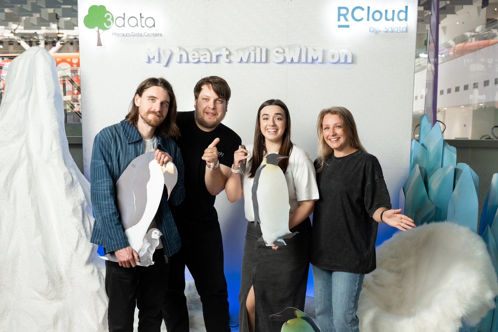 Четыре человека с картонными пингвинами на фоне стенда