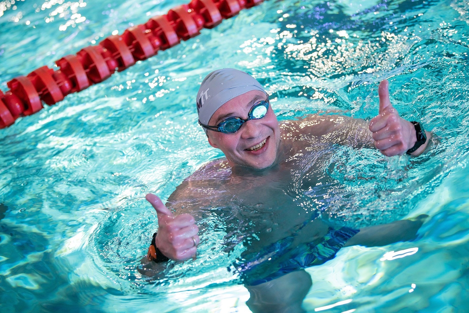 Улыбающийся пловец в воде, показывает оба больших пальца вверх