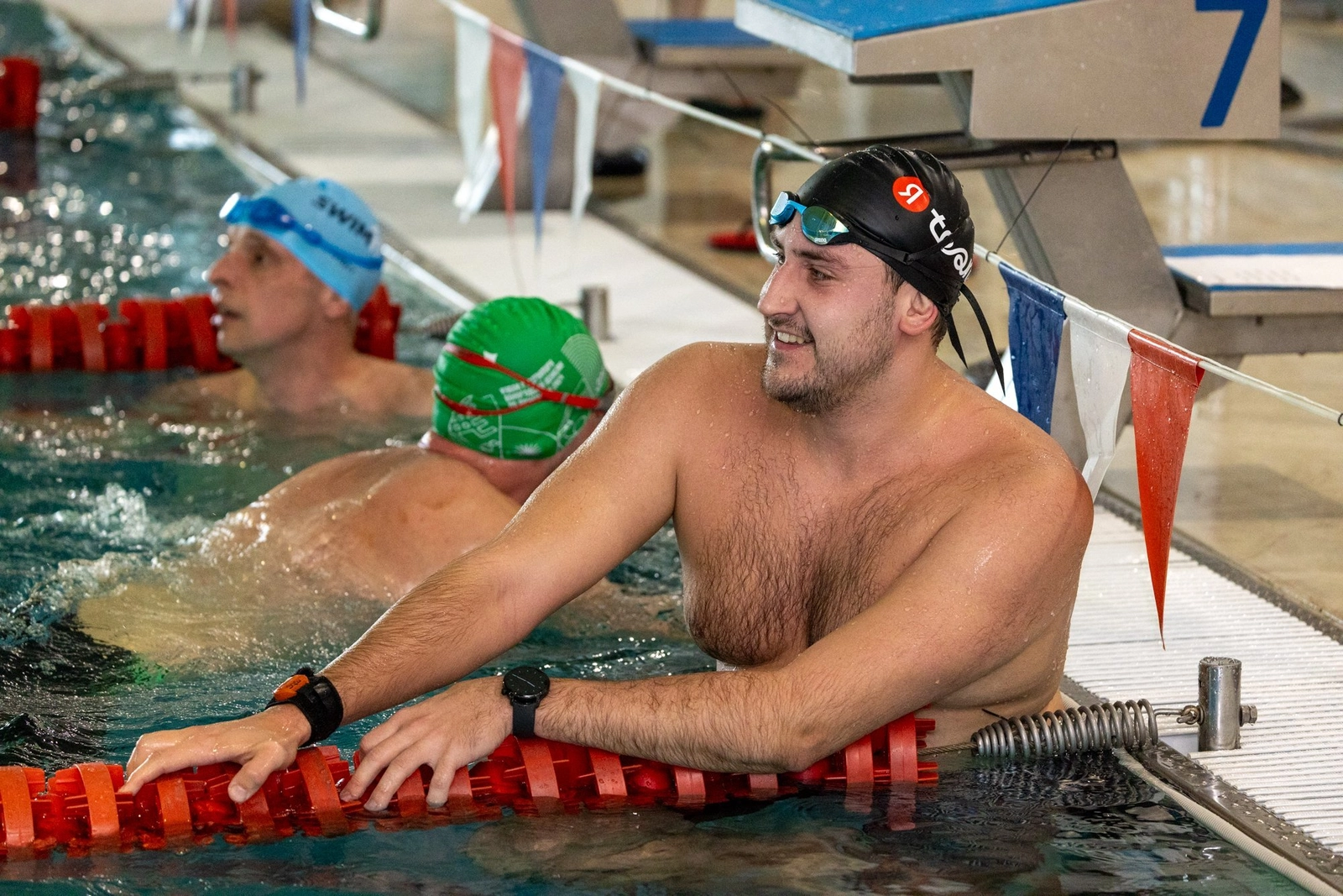 Улыбающийся пловец в воде у бортика, смотрит в сторону