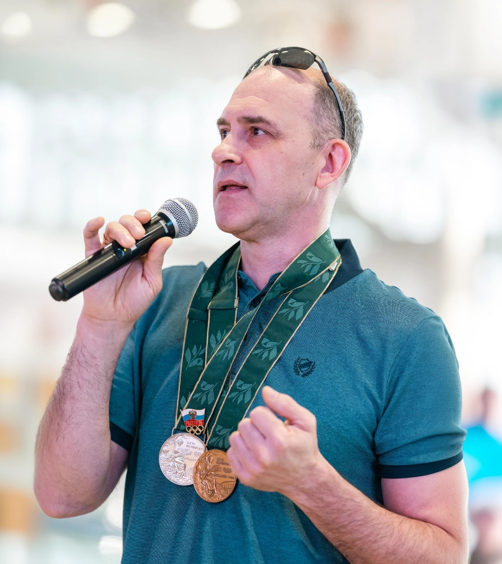 Владислав Куликов с микрофоном и медалями на шее выступает на мероприятии