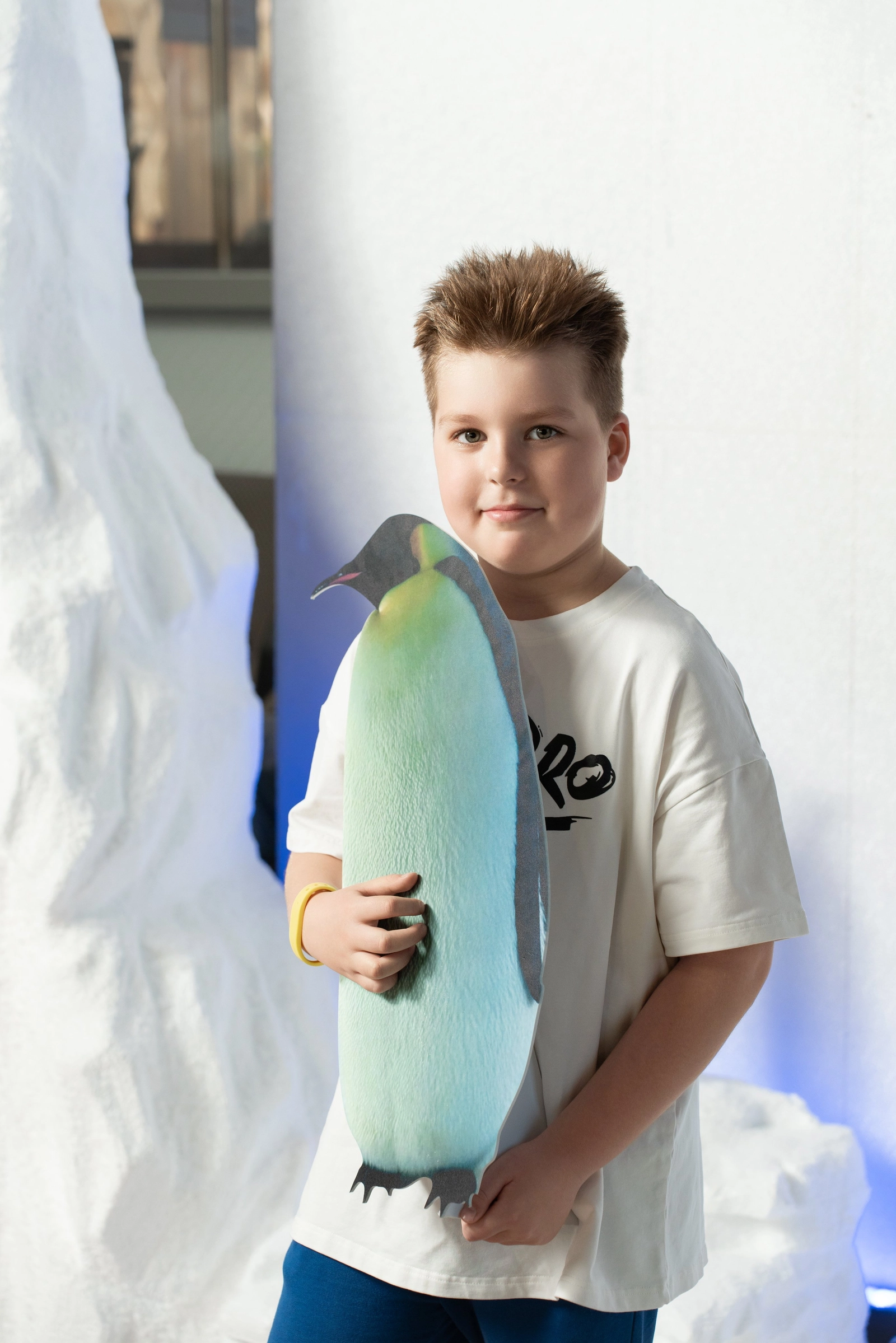 Мальчик держит картонного пингвина на белом фоне